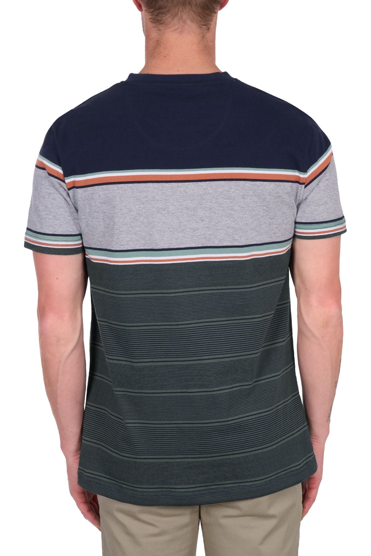 A man stands facing away from the camera, wearing a Thomas Cook Dion Tee—an all-cotton jersey tee featuring navy, gray, and green multi-colour stripes—and light-colored pants.