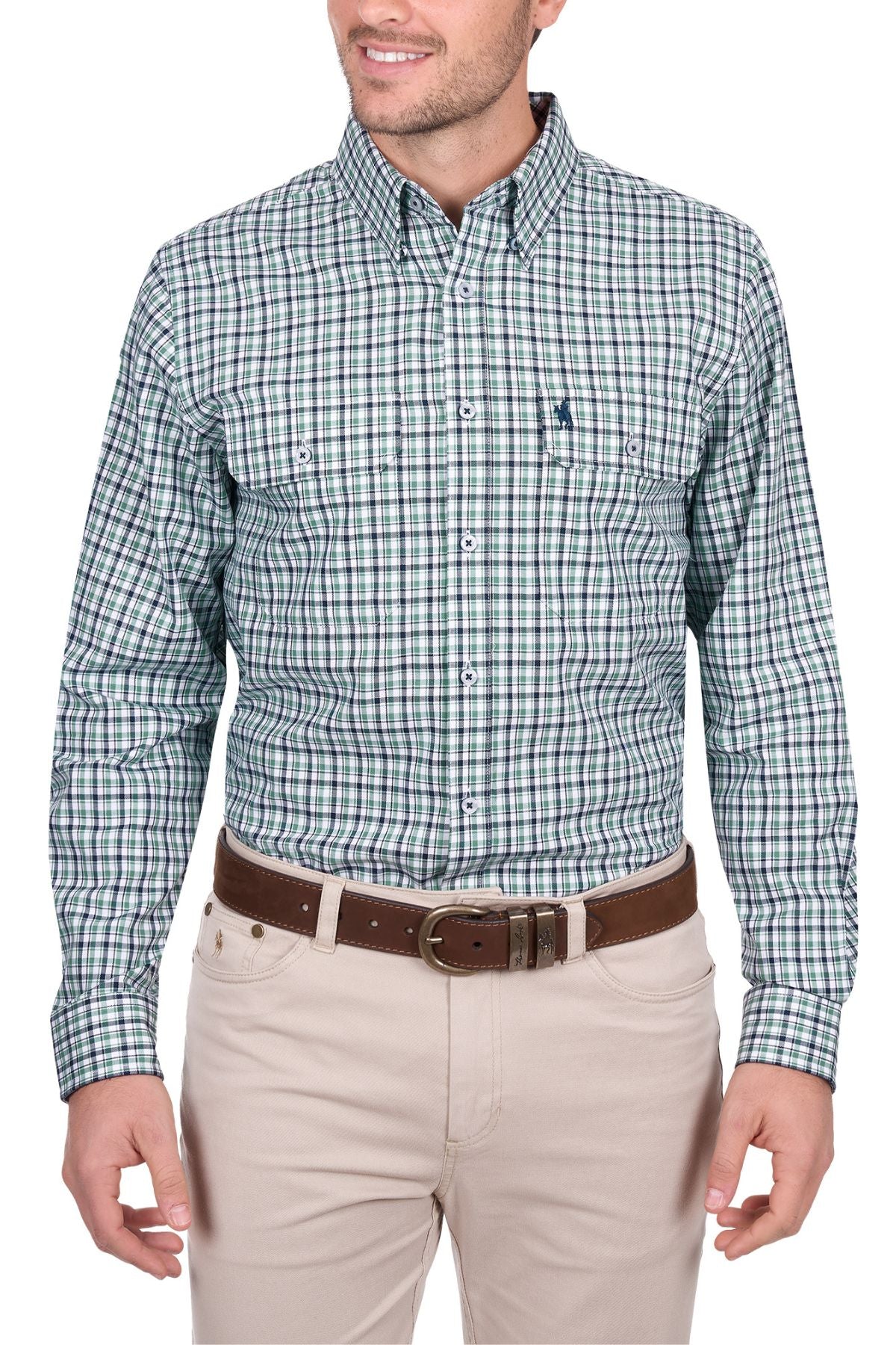 A man in a Thomas Cook Edward Shirt—a green, blue, and white plaid cotton long-sleeve—pairs it with beige pants and a brown belt. He stands relaxed, smiling, and facing slightly to the left.