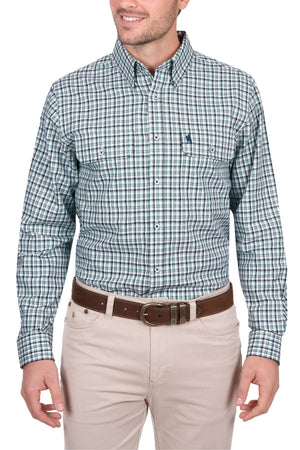 A man in a Thomas Cook Edward Shirt—a green, blue, and white plaid cotton long-sleeve—pairs it with beige pants and a brown belt. He stands relaxed, smiling, and facing slightly to the left.