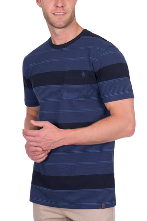 A man wears the Thomas Cook Edward Tee—a 100% cotton, multi-colour striped shirt with a chest pocket and embroidered logo—paired with light pants, standing against a white background, his face partially visible.