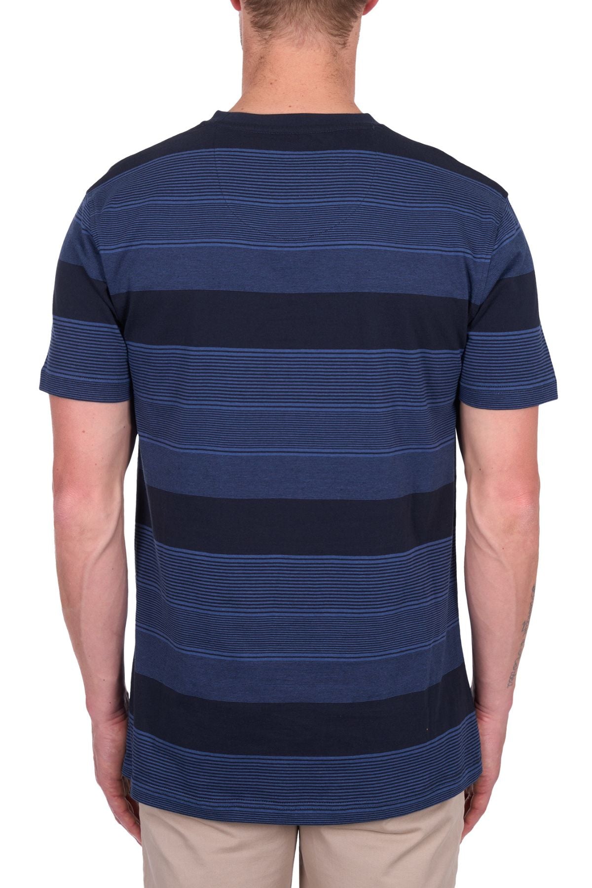 A person is seen from behind wearing the Thomas Cook Edward Tee, a short-sleeve navy blue t-shirt with light blue stripes in 100% cotton jersey, paired with beige pants against a plain white background.