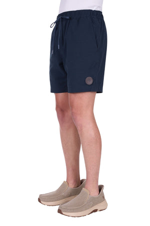 Wearing the Thomas Cook Felix Linen Short in navy, this person pairs them with a white shirt and beige slip-on shoes. The photo shows the outfit from the waist down, focusing on the shorts and footwear.