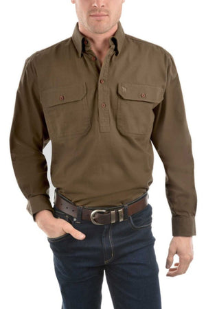 A man wearing a Thomas Cook Heavy Drill Half Placket Shirt with countryman pockets, dark blue jeans, and a brown belt stands with one hand in his pocket.