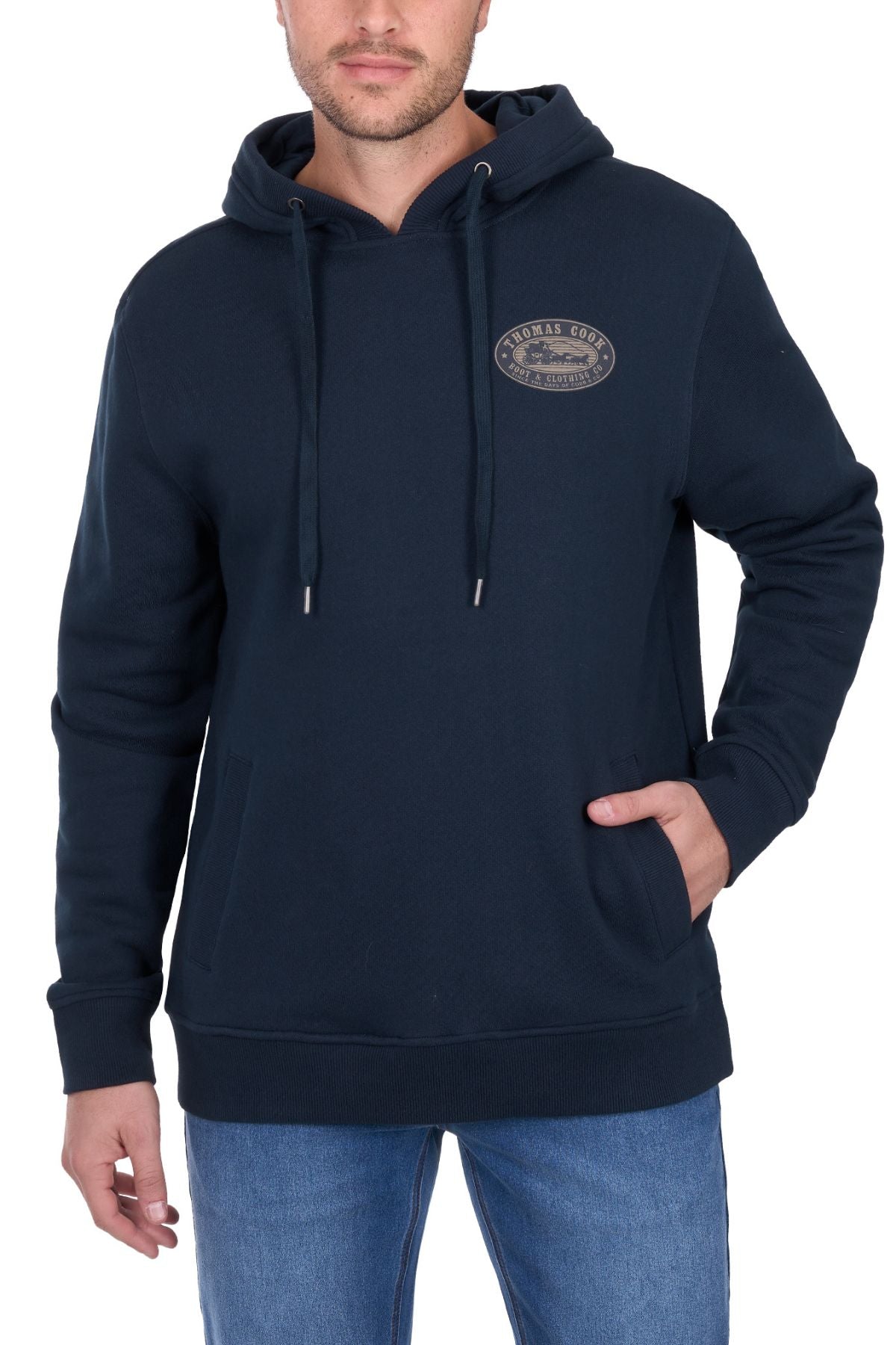 A man wears the Thomas Cook Heritage Oval Hoodie in dark blue, featuring a front pocket and small oval logo on the left chest, paired with light blue jeans, standing against a white background.