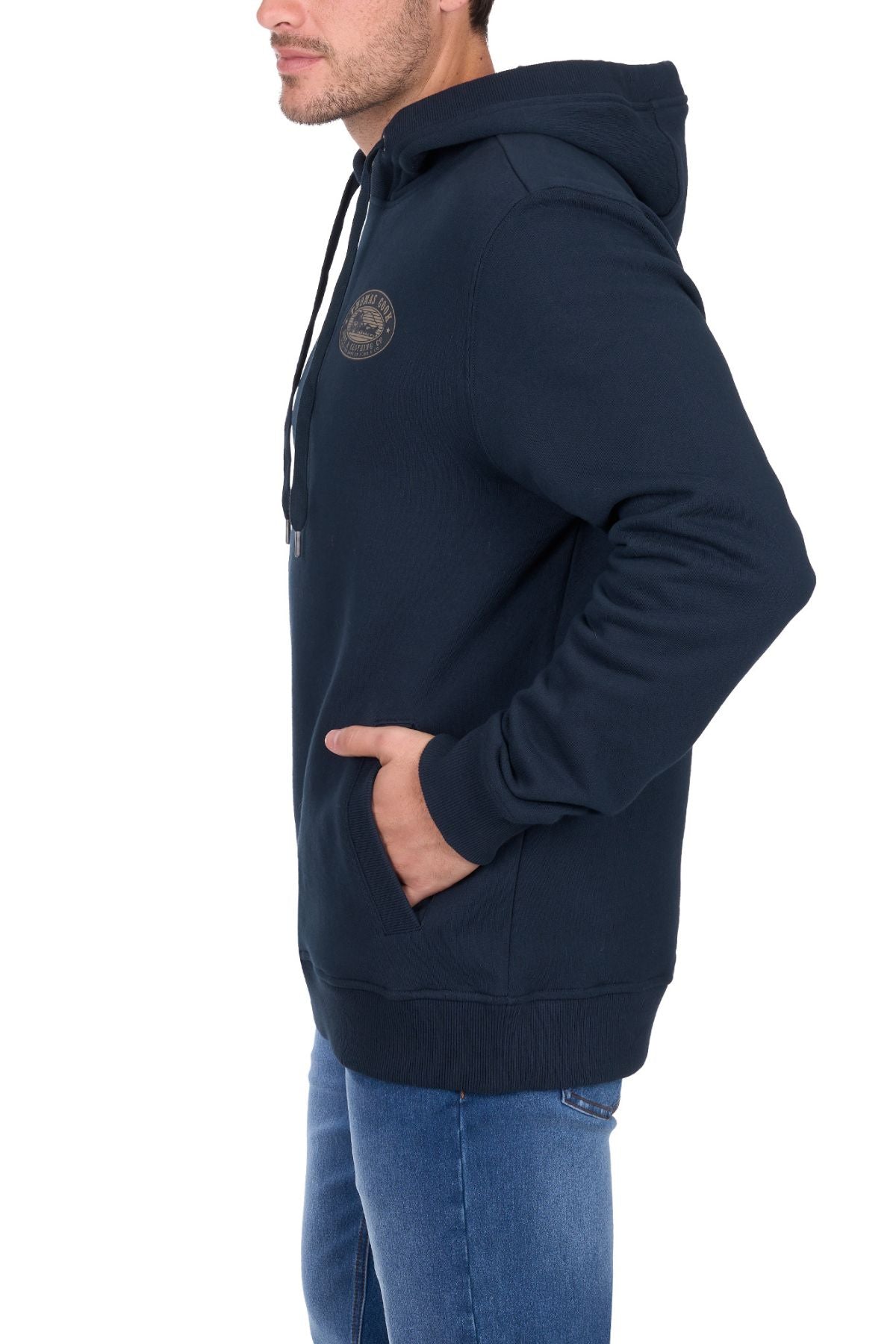 A person wears the Thomas Cook Heritage Oval Hoodie in dark blue with a chest logo and blue jeans, standing sideways with one hand in the hoodie pocket.