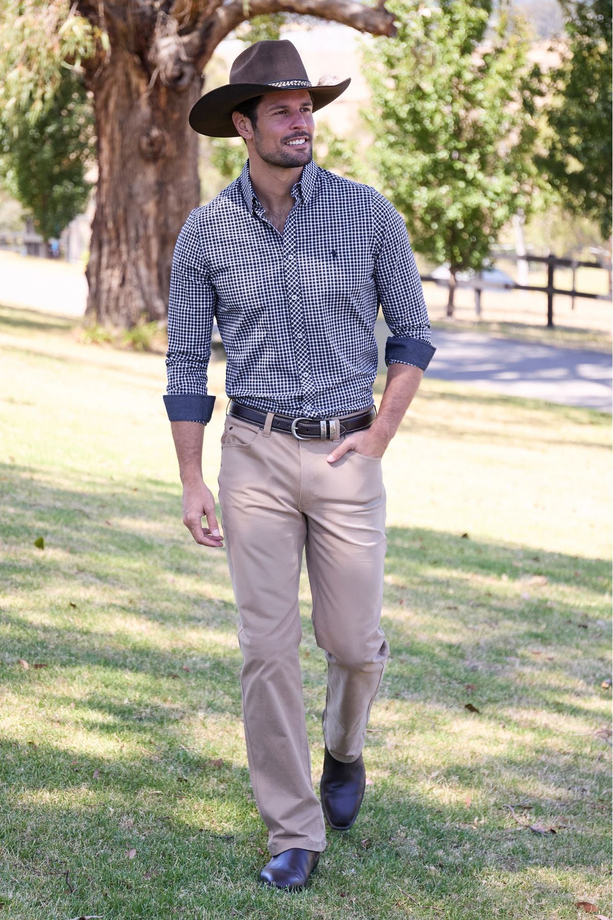 A man in the Thomas Cook Jason Tailored Shirt walks on park grass, smiling and looking to the side, with trees in the background.