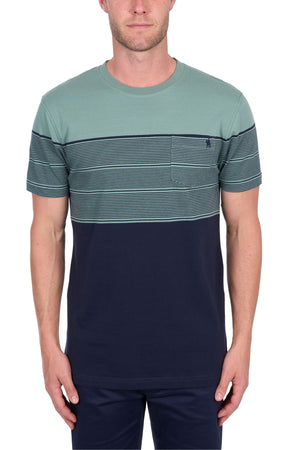 A man wears the Thomas Cook Jason Tee, made from 100% cotton jersey, with a solid dark blue bottom, blue and green striped top section, chest pocket, and matching dark blue pants, standing against a white background.