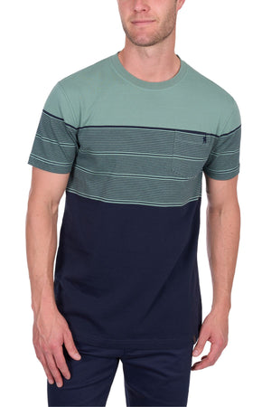 A man stands with one hand by his side, wearing the Thomas Cook Jason Tee: a short-sleeve, 100% cotton crew-neck T-shirt featuring a green top, multi-colour chest stripes, small chest pocket, and solid navy bottom panel.