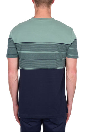 A man is seen from the back wearing the Thomas Cook Jason Tee, a 100% cotton jersey with a light green upper, multicolour horizontal stripes in the center, and a solid dark blue lower section. He also wears dark pants.