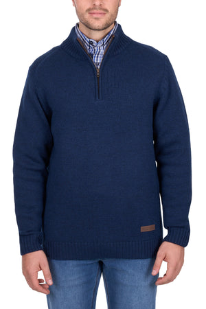 A man wears the Thomas Cook Jesse 1/4 Zip Jumper in navy blue, with a chunky rib knit and half-zip collar, layered over a blue and white plaid shirt and paired with blue jeans, standing against a white background.