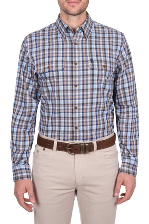 A man wears a Thomas Cook Jonathan Shirt in blue, brown, and white plaid—100% cotton with two chest pockets—paired with beige pants and a brown belt, standing facing forward.