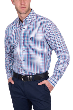 A man wears the Thomas Cook Joseph Shirt, a long-sleeved, button-up plaid made from 100% cotton in blue, white, and red. It’s tucked into navy pants with a black belt; his hands are in his pockets and his face is partially out of frame.