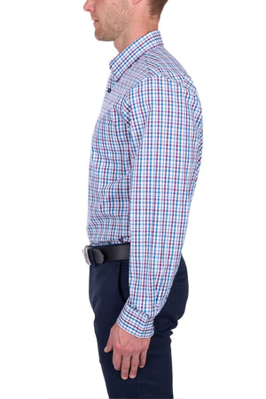 A man stands in profile wearing the Thomas Cook Joseph Shirt, featuring a blue, red, and white checkered 100% cotton fabric, paired with navy trousers and a black belt, set against a plain white background.