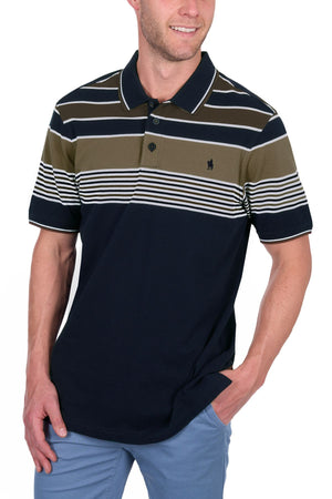 A man wearing the Thomas Cook Josua Polo, a navy blue 100% cotton pique shirt with white, olive, and black stripes, paired with light blue pants. He smiles with one hand in his pocket.