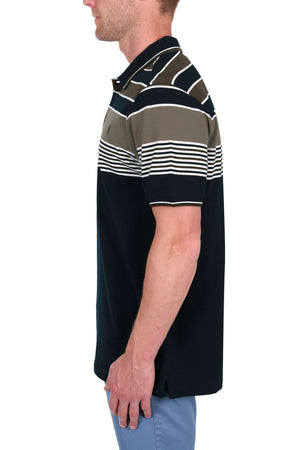 A man models the Thomas Cook Josua Polo, featuring 100% cotton pique in white, brown, and black stripes. He stands sideways in light blue pants against a plain white backdrop.