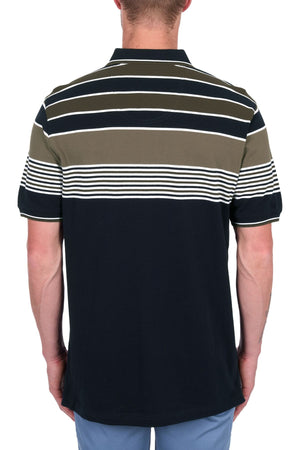 A man faces away, wearing the Thomas Cook Josua Polo—100% cotton pique with horizontal white, olive, and navy stripes—paired with light blue pants, set against a white background.