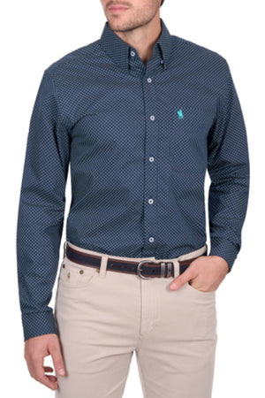 A man wears the Thomas Cook Kevin Shirt in navy with a small geometric pattern, paired with beige pants and a dark belt. Suitable for work or casual wear, he stands slightly turned, one hand in his pocket.