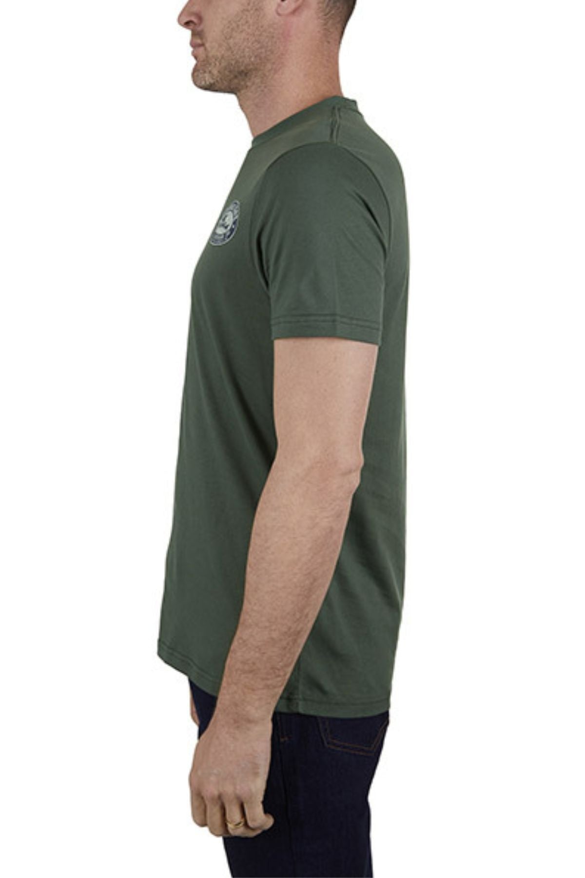 A man stands in profile facing left against a white background, wearing a green 100% cotton Thomas Cook Oval Tee (classic fit) and dark jeans.