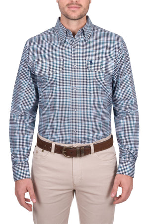 A man wearing the Thomas Cook Stephen Shirt, a blue and white checked 100% cotton men's work shirt, with tan pants and a brown belt stands against a white background.
