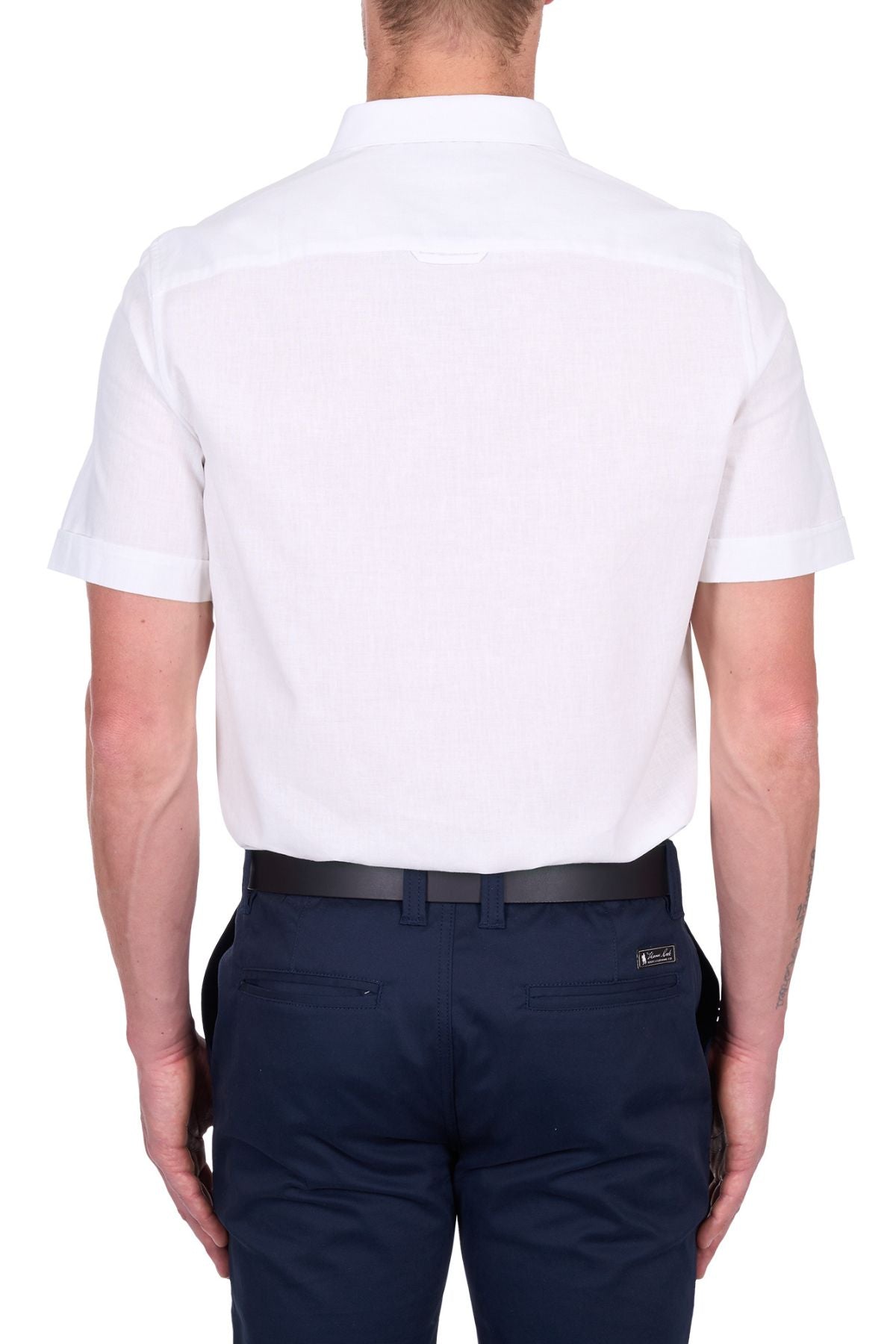 A man seen from behind wears the Thomas Cook TC Linen Short Sleeve Shirt, a summer essential, tucked into dark navy blue pants with a black belt. The background is plain white.
