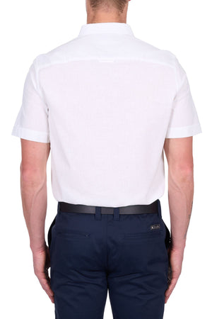 A man seen from behind wears the Thomas Cook TC Linen Short Sleeve Shirt, a summer essential, tucked into dark navy blue pants with a black belt. The background is plain white.