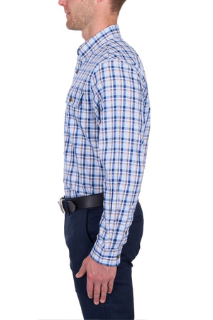 A man in profile wearing the Thomas Cook Thomas Shirt—blue, white, and brown cotton checks with long sleeves—paired with dark pants and a black belt, stands against a white background.