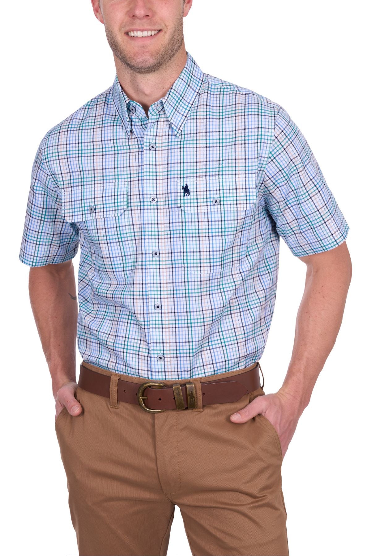 A man wears the Thomas Cook Matt Short Sleeve Shirt—a button-up cotton shirt with blue, green, and white plaid—tucked into tan pants with a brown belt. Smiling, he has his hands in his pockets.