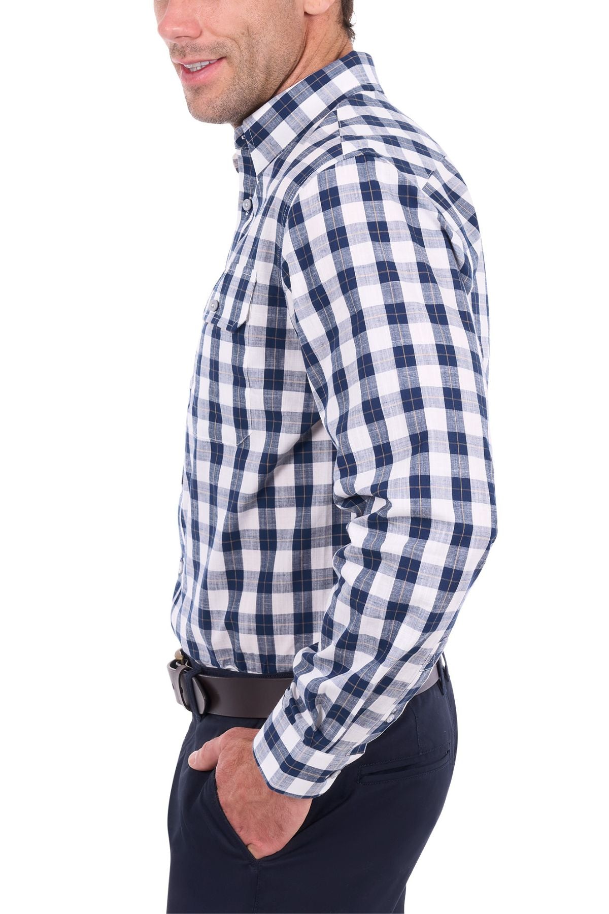 A man stands in profile against a white background with one hand in his pocket, wearing the Thomas Cook Ezra Shirt—a blue and white checked cotton shirt—and dark pants.