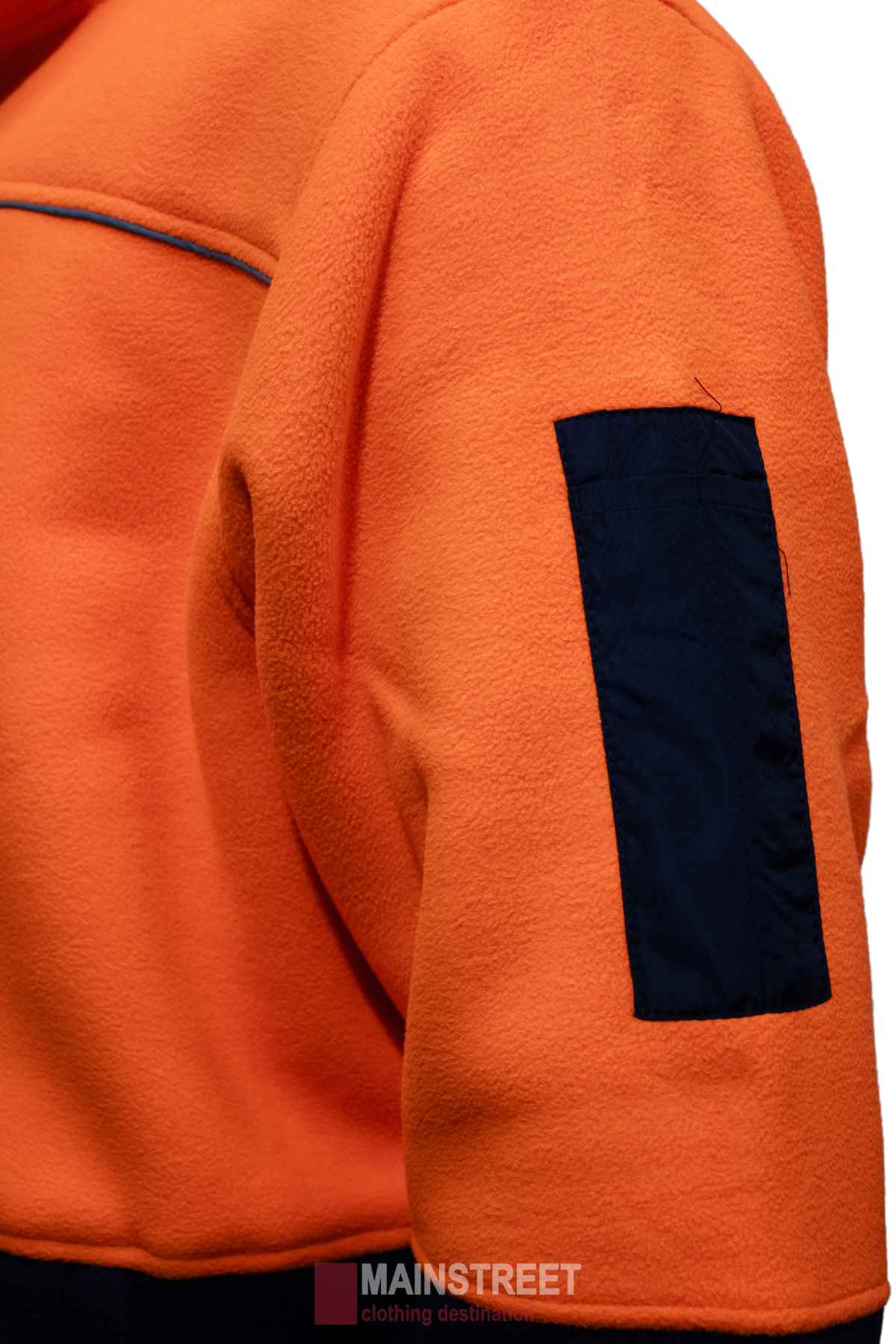 Close-up of an orange MakRear Sherpa Polar Fleece Jacket with a navy blue sleeve patch. Made from durable polyester, it features a textured fabric and full zip front. The "Mainstreet - clothing destination" logo is partially visible at the bottom.