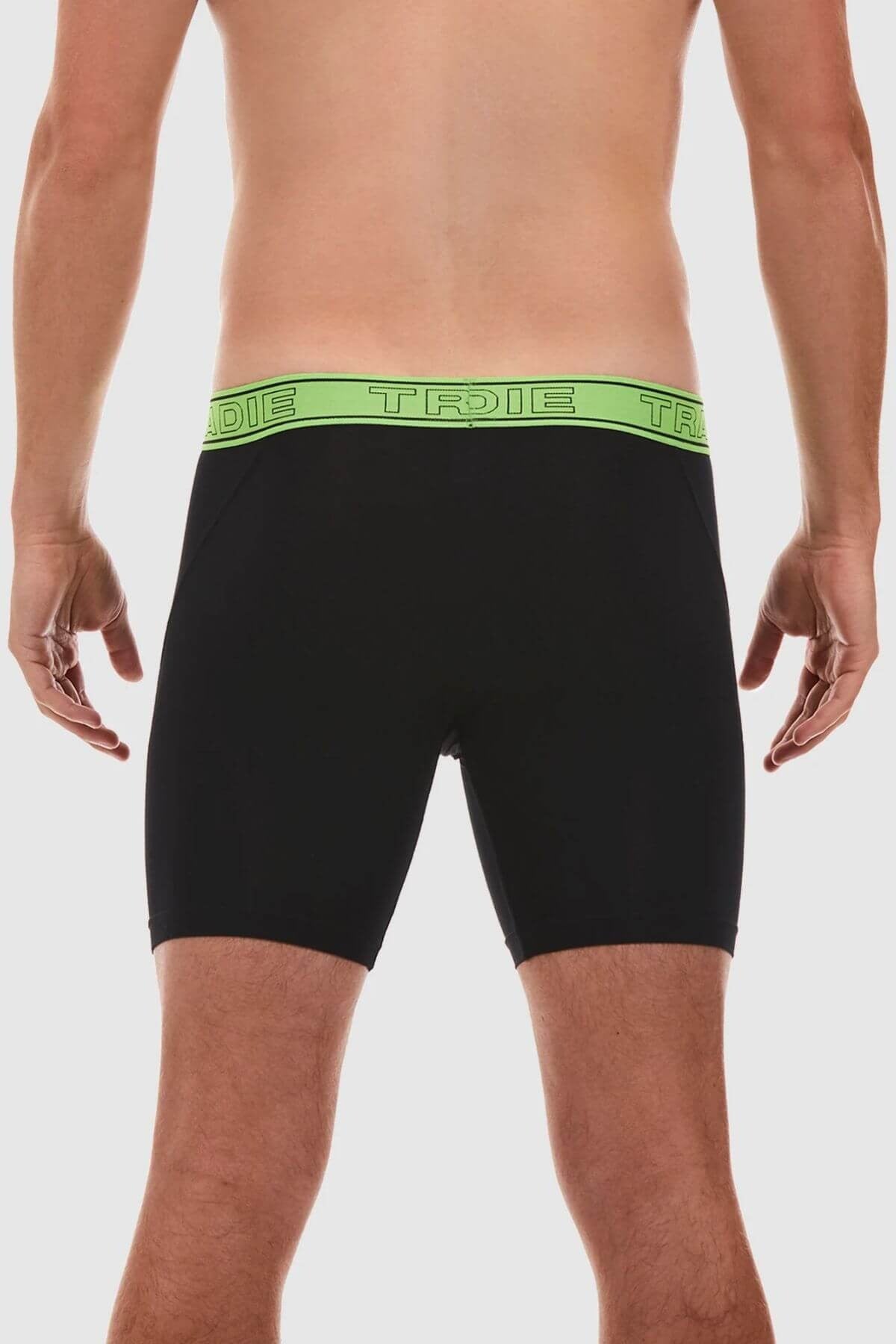 A man is standing with his back to the camera, sporting Tradie Bamboo No Chafe Long Leg Trunks in black. The trunks feature a neon green waistband that repeatedly displays the word "TRADIE." Made from breathable stretch material, these trunks provide both comfort and style. The background is plain white.