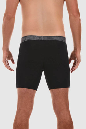 A person stands with their back to the camera, wearing black Tradie Bamboo No Chafe Long Leg Trunks featuring an elastic waistband that has "TRIDE" written on it in a repeated pattern. The person is shirtless, showcasing their bare back and legs against a plain white background. The trunks are made from breathable stretch material for ultimate comfort.