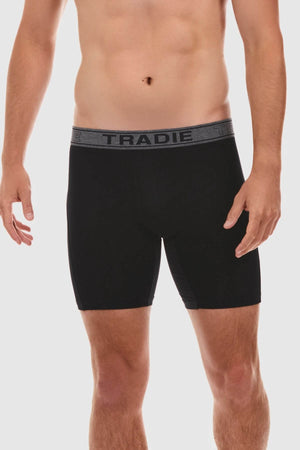 A person is standing and wearing Tradie Bamboo No Chafe Long Leg Trunks in black, featuring a gray waistband with the word "TRADIE" written on it. The photo captures the individual from mid-thigh to just below the chest against a plain white background, emphasizing the breathable stretch material that ensures ultimate comfort.