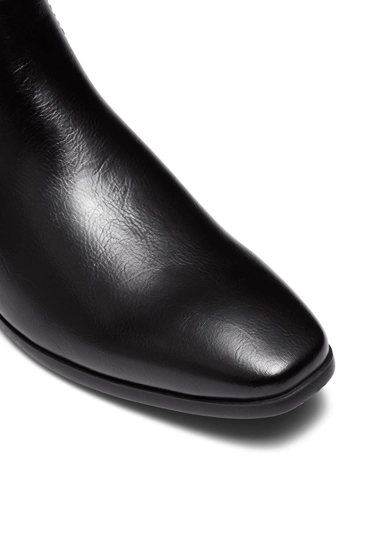 Close-up of the toe of the UNcut Newlands Boot, a sleek black leather shoe with a shiny finish and an almond toe shape, set against a white background.