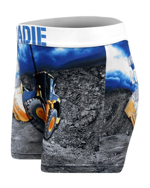 The Tradie Mens Work N Surf Trunk features a yellow construction loader print on rocky terrain with a blue sky, a white waistband, and quick-drying fabric for cool comfort all day—perfect for work or play.