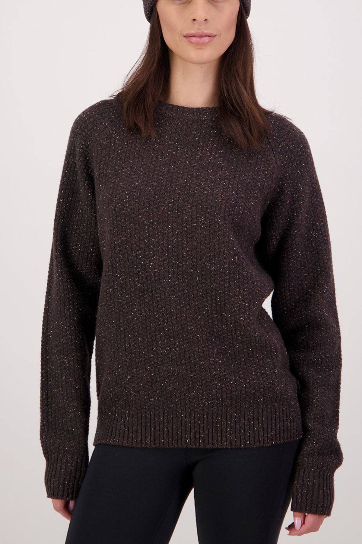 Wearing the Swanndri Lyttelton Womens Waffle Crew in dark brown with black pants and a dark knit beanie, a woman with long, dark hair stands against a plain light background.