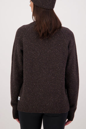 A person with long brown hair wears a brown knit beanie and the Swanndri Lyttelton Womens Waffle Crew, standing with their back to the camera against a plain light background.