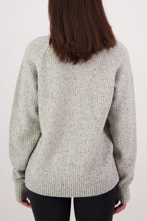 A woman with straight brown hair is seen from behind, wearing a light grey Swanndri Lyttelton Womens Waffle Crew sweater and dark pants against a plain light background.