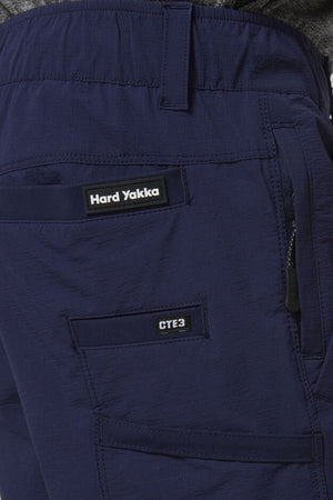 Close-up of a person wearing Hard Yakka X Range Mid Short in navy blue, featuring the brand label, a zippered utility pocket, and a "CTE3" pocket on the upper thigh.