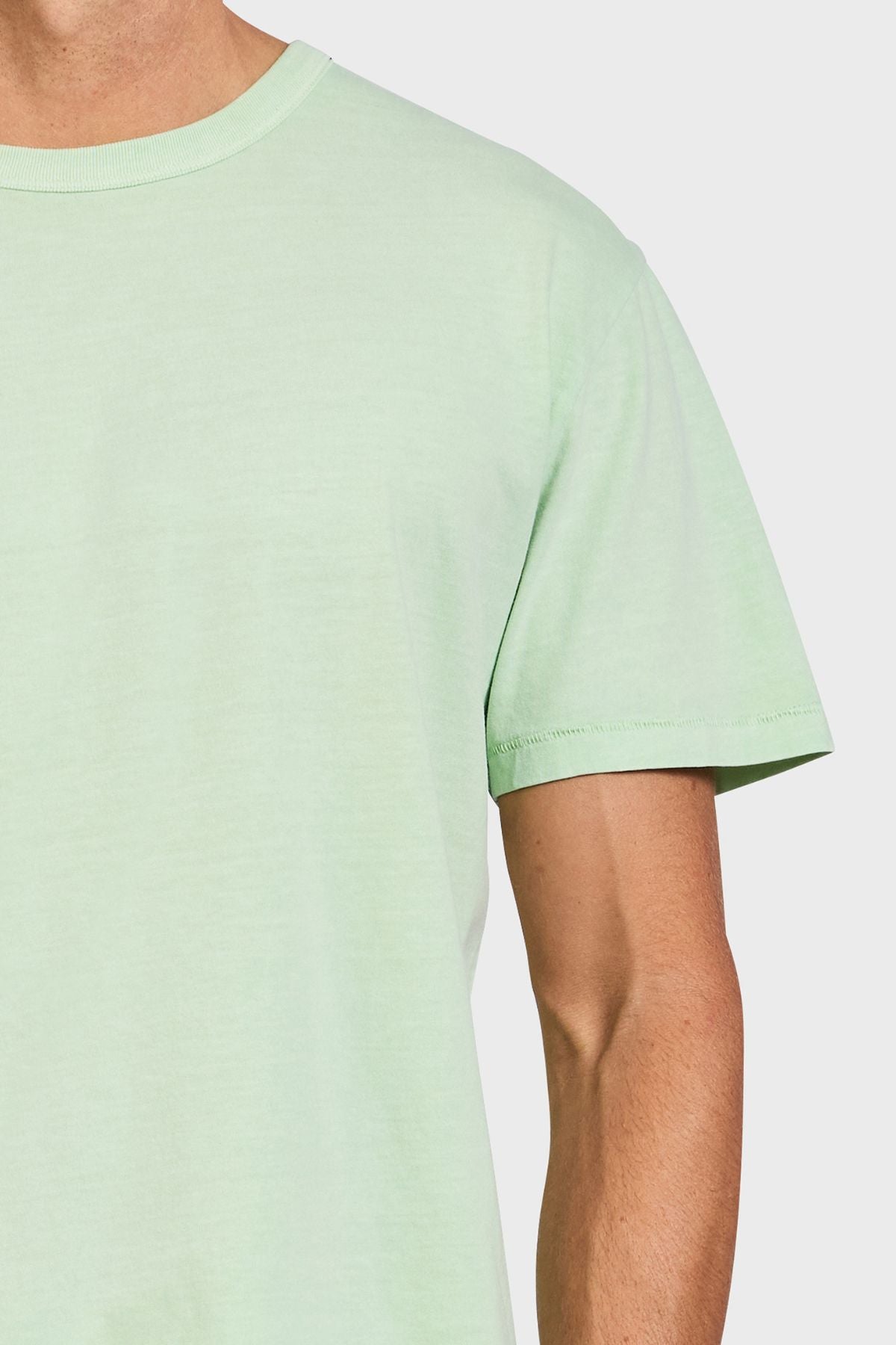 A person wears the Academy Brand Jimmy Tee in light green, a 100% cotton loose fit t-shirt, shown from shoulders to upper arms against a plain white background.