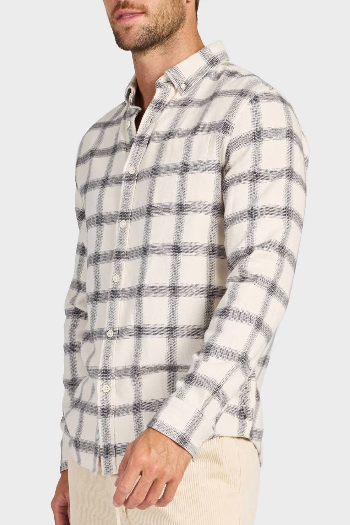 A man wearing an Academy Brand Buhler Shirt in cream with a gray plaid yarn-dye twill pattern and beige pants, shown waist up against a plain background.