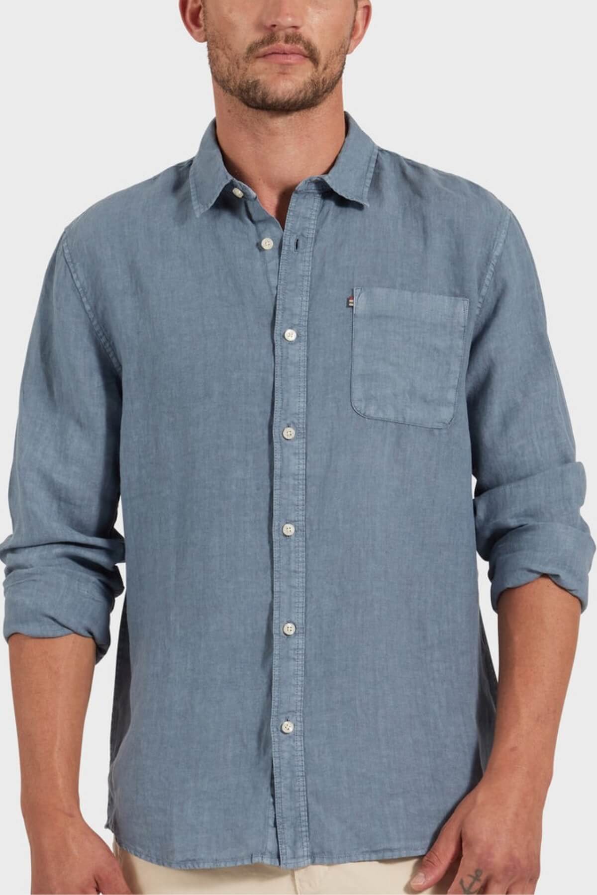 A man in the Academy Brand Hampton Linen Shirt, light blue with a front pocket and rolled-up sleeves, stands against a plain light background.