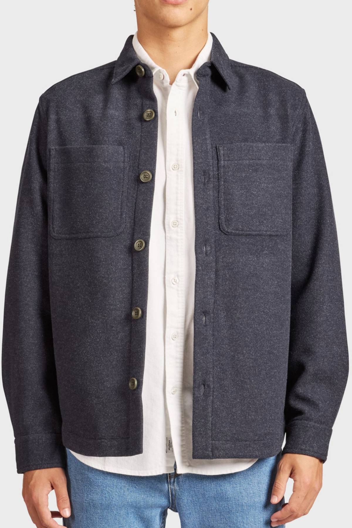 A person wears the Academy Brand Lloyd Overshirt, a dark gray men's overshirt with two chest pockets, styled over a white shirt and blue jeans. The jacket is partly unbuttoned and the person's face is not shown.