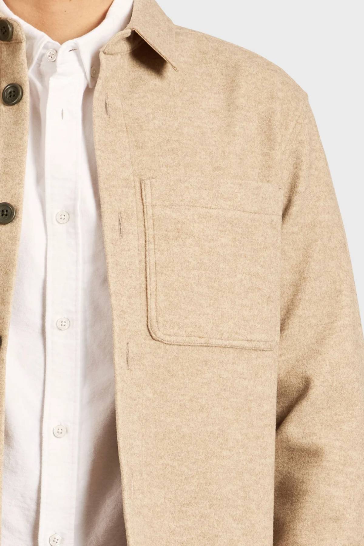 A man wears the Academy Brand Lloyd Overshirt—a beige, button-up men’s overshirt with a chest pocket—over a white shirt, shown from neck to mid-torso against a plain background.
