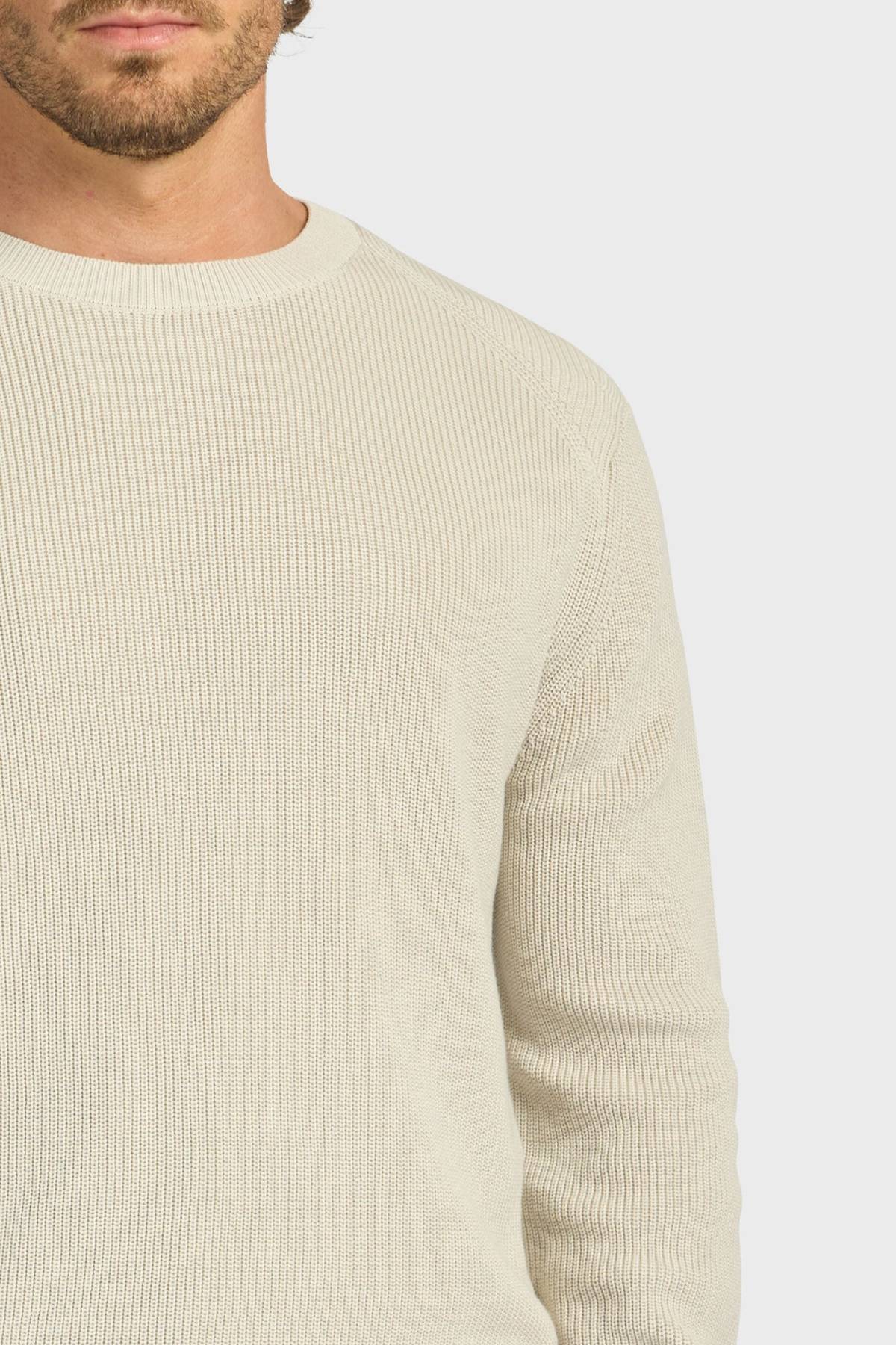 Cropped image of a man wearing the Academy Brand Oliver Knit Crew—a light beige, ribbed cotton sweater with long sleeves—shown from shoulders to waist against a neutral background.