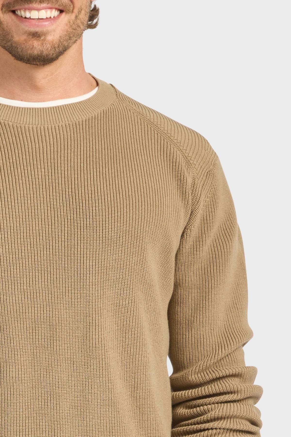 Wearing the Academy Brand Oliver Knit Crew in beige premium cotton ribbed knit over a white shirt, a smiling man’s lower face and upper torso are shown against a light background.