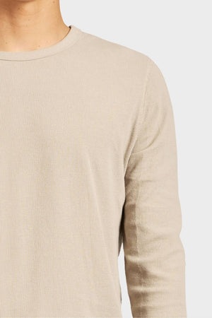 A close-up of a person wearing the Academy Brand Workers Crew, a light beige, durable long-sleeve French rib crew neck shirt. Only the shoulder, chest, and partial neck are visible against a plain white background.