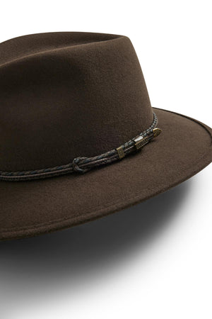 A close-up of the Akubra Traveller, a brown felt hat featuring a braided dark band and small metallic tag, set against a white background.