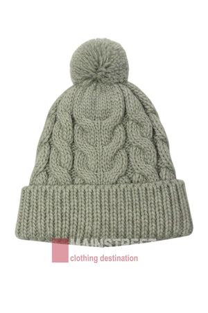 The Anticorp Ladies Cable Lined Beanie is a light gray women’s beanie with a chunky cable knit, folded brim, and playful pom-pom. "MAINSTREET clothing destination" appears partially at the bottom.