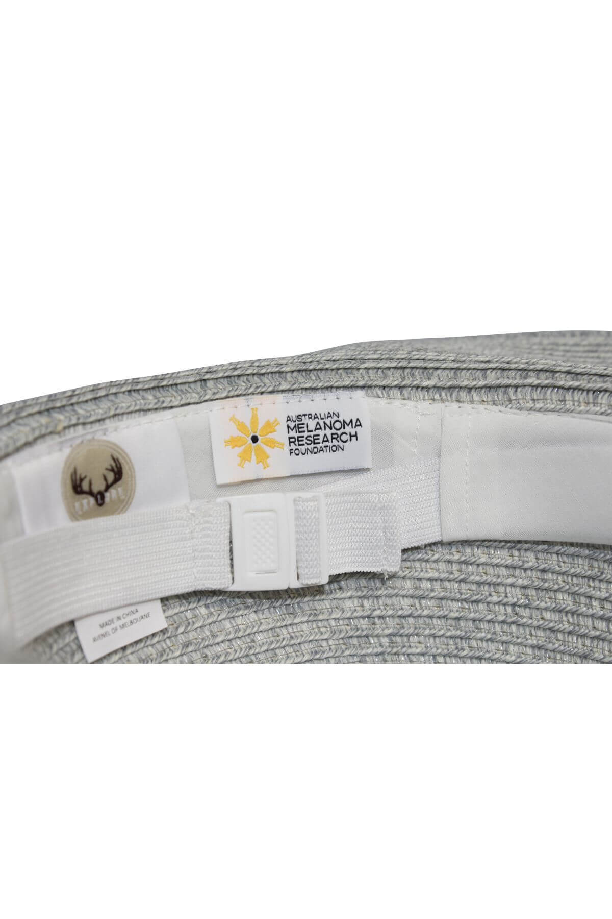 Close-up of the inside of an Avenel Crushable Two Tone Safari Traveller hat in light grey, featuring labels for "Australian Melanoma Research Foundation" and a small button with a deer head design.