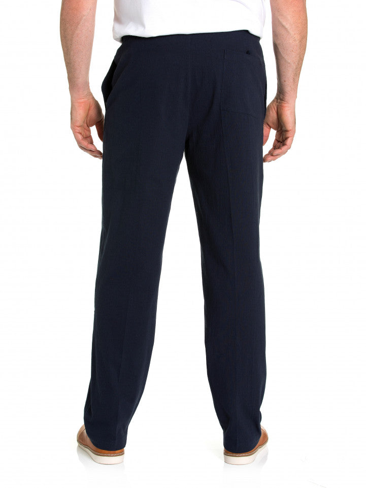 A person wearing casual black Breakaway Crinkle Pants with an elastic waist and a white shirt is standing with their back facing the camera. They are also wearing light brown shoes and are standing against a plain white background.